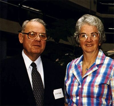 A man in a dark suit posing next to a woman in a plaid shirt